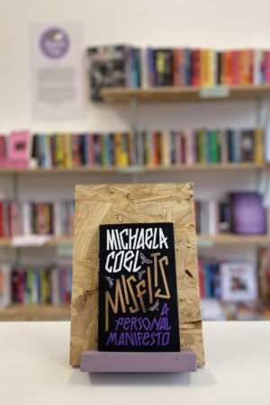 Copi o 'Misfits' yn sefyll ar stondin llyfrau, tu blaen silffoedd o lyfrau yn y cefndir.