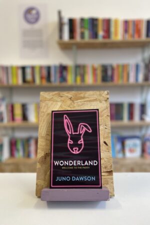 Copi o 'Wonderland' yn sefyll ar stondin llyfrau, tu blaen silffoedd o lyfrau yn y cefndir.