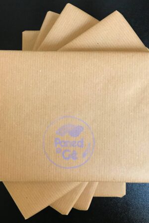 Pentwr o barseli brown ar gefndir du. Ar y parsel ar ben y pentwr, mae logo Paned o Gê wedi printio mewn lafant.