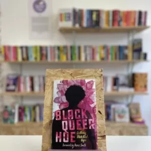 Copi o 'Black Queer Hoe' yn sefyll ar stondin llyfrau, tu blaen silffoedd o lyfrau yn y cefndir.